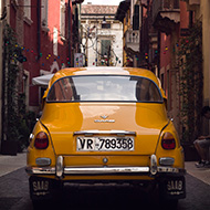 Old mustard yellow car down a narrow Italian side street