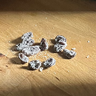 A bowl of muesli sat on a kitchen work surface. Next to the bowl are a handful of raisins that have been picked out and placed to one side.