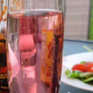 Picture taken outdoors on a sunny day, a plate of fresh salad, and roasted veg and chicken is surrounded by a cool glass of water and condiments.