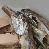 A small ceramic bowl contains a mix of tiny silver fish and flakes of toasted almond alongside is the shiny packaging covered with Japanese writing and a picture of the fish and almonds