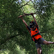 A small boy wearing shorts and a life jacket holding on to a rope swing, swinging out over the river thames