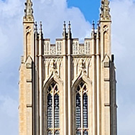 Ruins of the old Abbey. Two tall stone columns stand taller than the other ruins. They almost look like two rabbits standing on hind legs with their front paws clasped together in prayer. The Cathedral can be seen in the background between them.