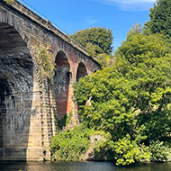 Large stone viaduct over river with trees in sunshine