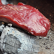 A rare beef flank lies on charcoal in a fire pit