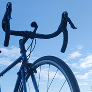 A blue racing bike is perched on the roof of a car, on a sunny morning with rolling hills in the background.