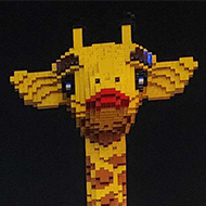A life size giraffe made out of lego stands out against the night sky
