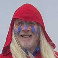 Man in red cloak with blue face paint and a hand drum