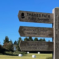 A wooden sign post in a field next to a plinth marking the source of the river thames