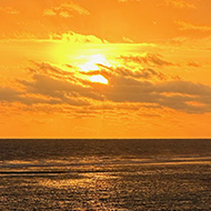 Orange sunset with some clouds banding. Open water and beach at bottom with people silhouetted as small figures.