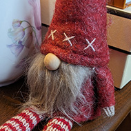 A felt bearded dwarf, dressed in red, sat on a table next to a mug