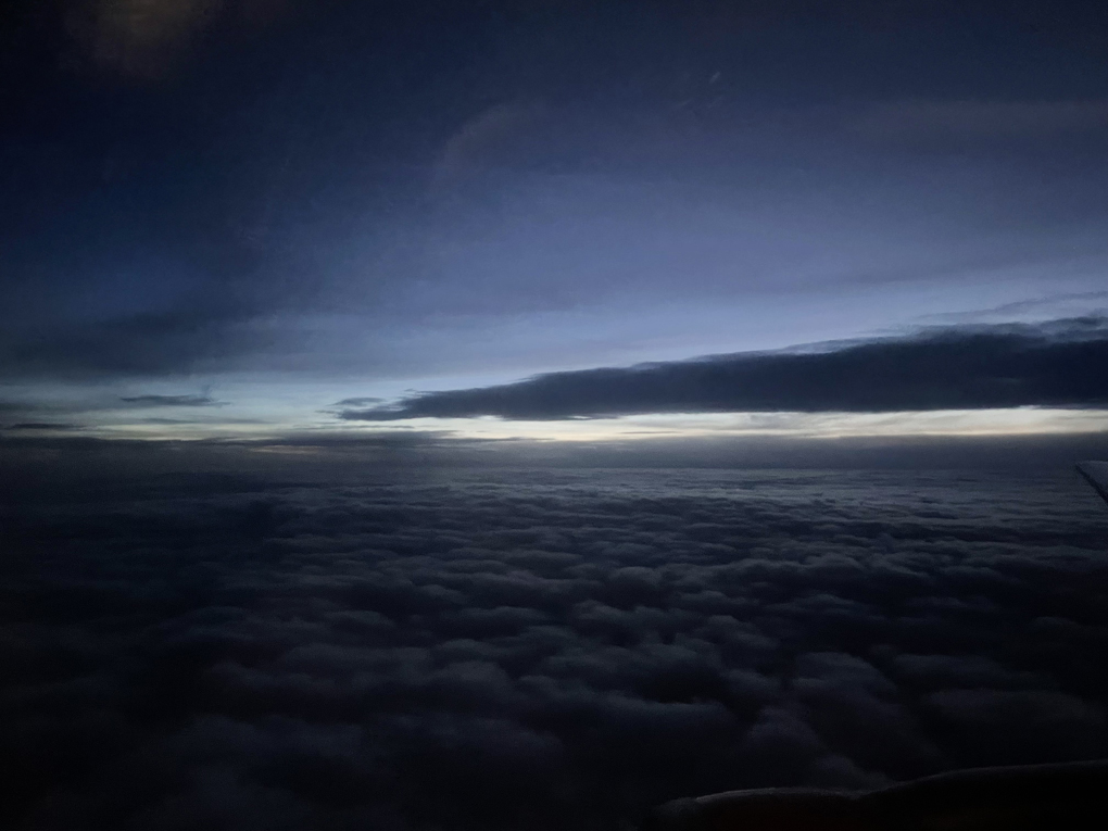 Image taken from the window of a plane showing dark clouds with sunlight on the horizon