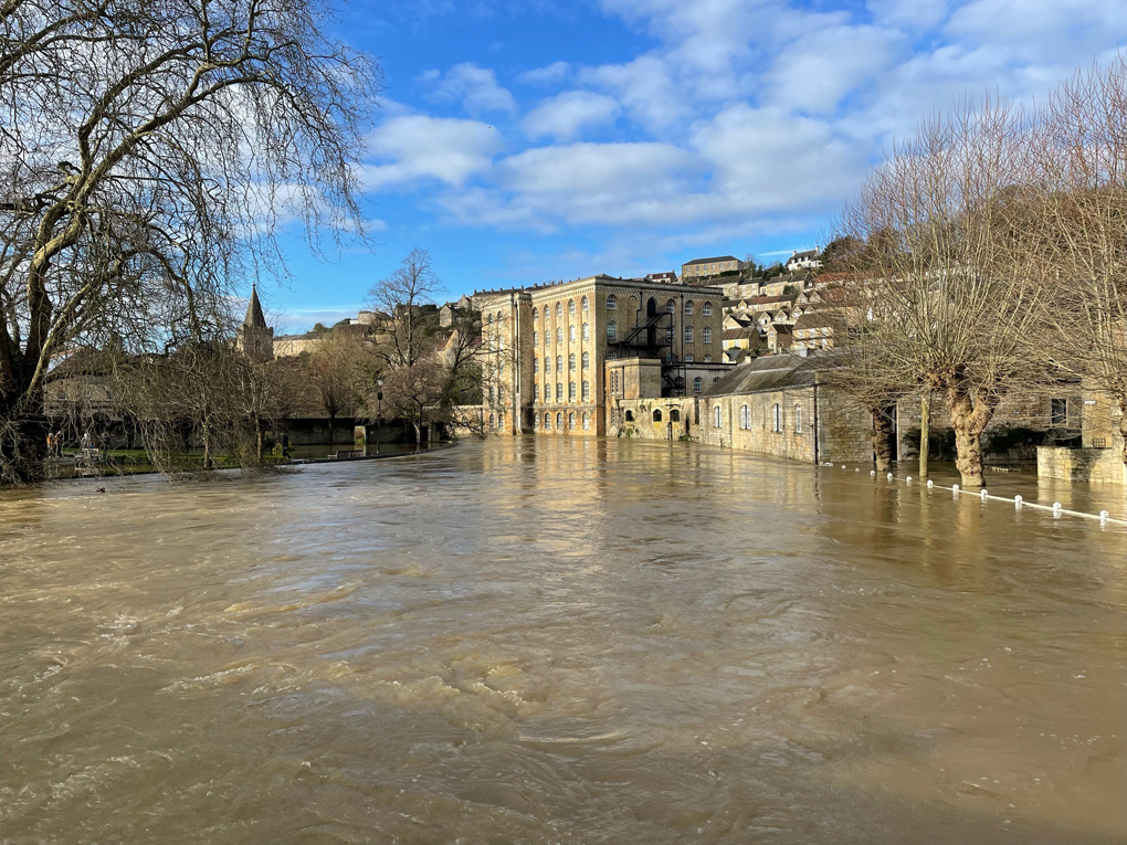 A river flooded into roads and parkland with an old mill in the background