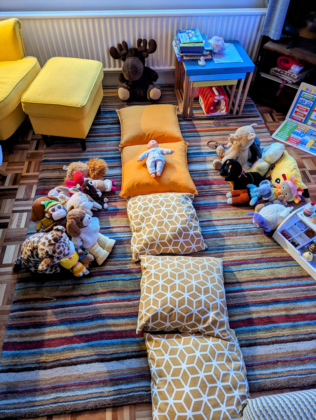 Baby doll on a cushion surrounded by other plush toys