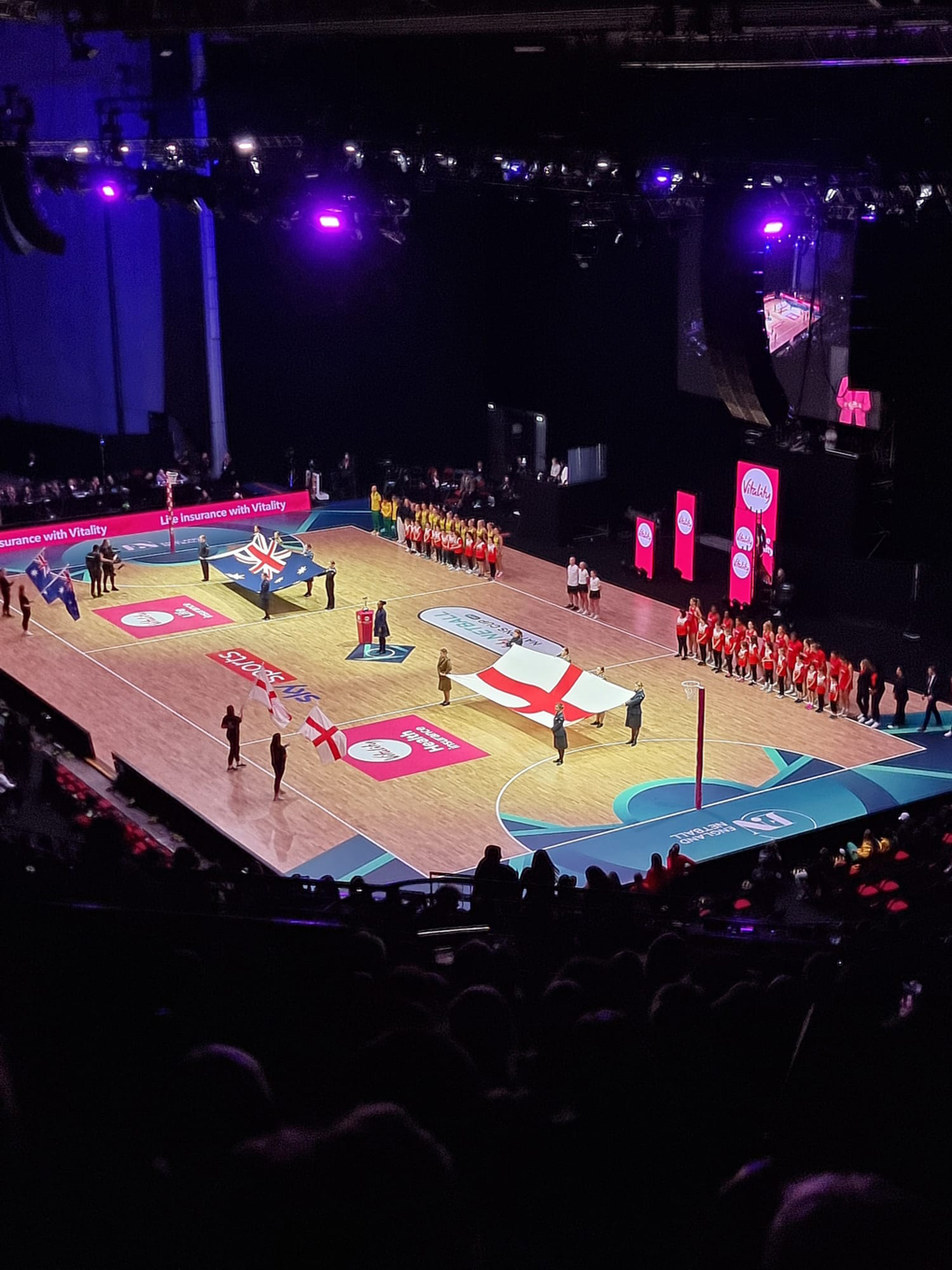 View over netball court before the game with English and Australian flags held out.