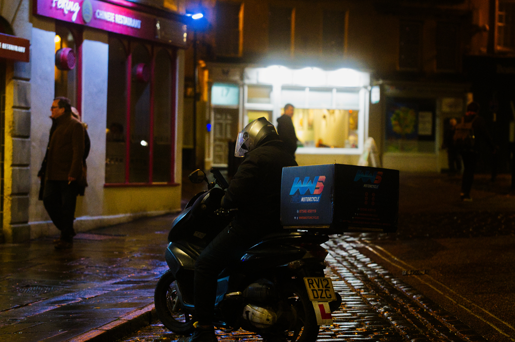 A delivery driver stationary on his scooter, waiting for their next delivery app job.