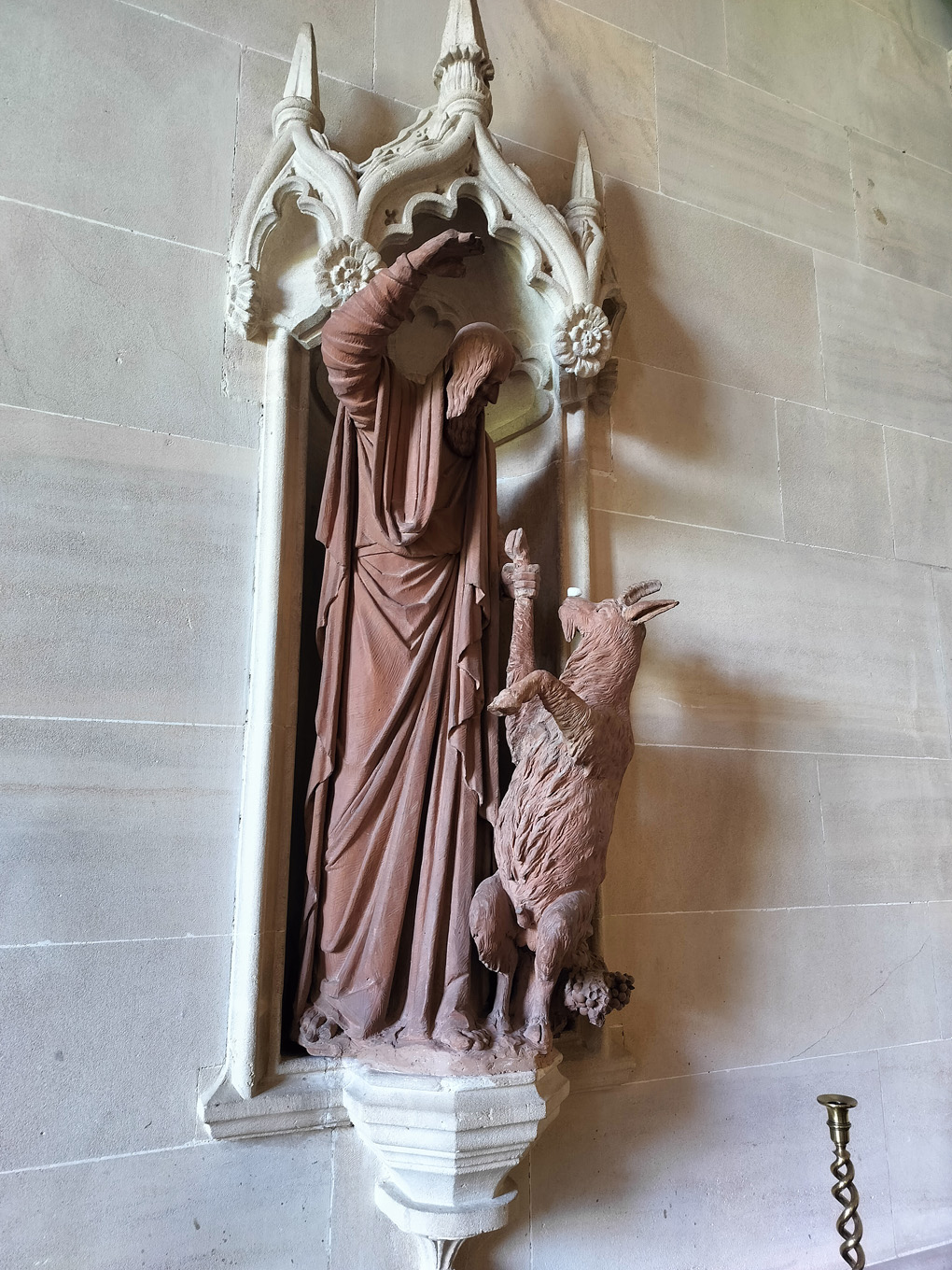 A statue, set into a wall, of a man and a goat. The goat is on its hind legs and a sugar lump has been balanced on its nose.