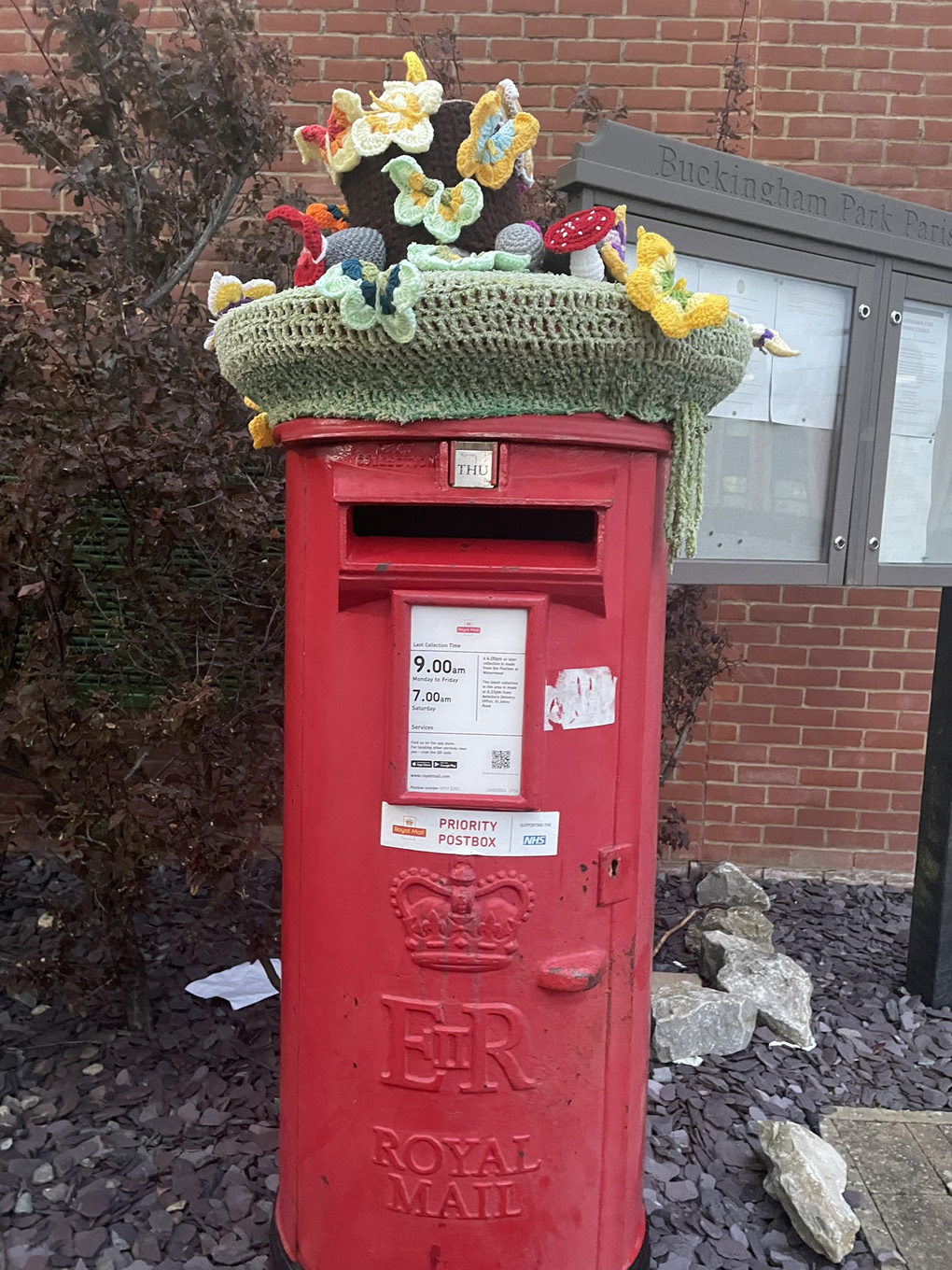 Red Royal Mail post box with a knitted topper.