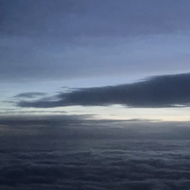 Image taken from the window of a plane showing dark clouds with sunlight on the horizon