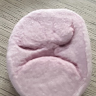A pink marshmallow sat on a wooden office desk. The marshmallow has a grumpy face.