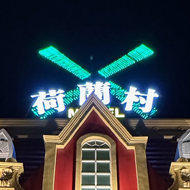 A Dutch windmill themed motel front with neon lights. Predominantly red and yellow. Two arches for car going in and out.