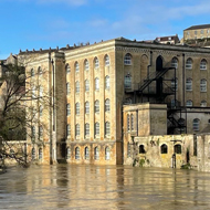 A river flooded into roads and parkland with an old mill in the background