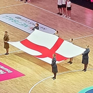 View over netball court before the game with English and Australian flags held out.