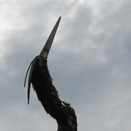 An ironwork sculpture of a heron (I think!) balances precariously against a bright sky.