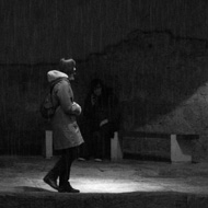 A lone woman steps into a pool of light in the Roman Baths, while in the foreground rain is falling into the main bath's water