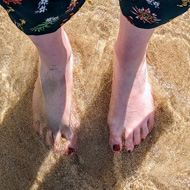 A view down to my feet partially buried in sand and with bright clear waves washing over them
