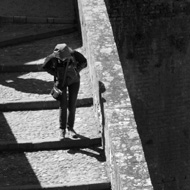 A black and white photo of two tourists walking down old stars, one framed in a sharply defined triangle of light