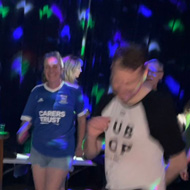 Lots of people lit only with coloured lights dancing in a dark room