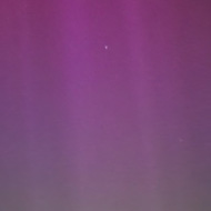 A sky fading from pink to purple to green over a tiled roof