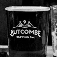 Black and White image with a single singer/guitarist at the mic in the middle ground but a shallow depth of field throws him out of focus with on the beer on the table at the front of the image being the only sharp part of the frame.