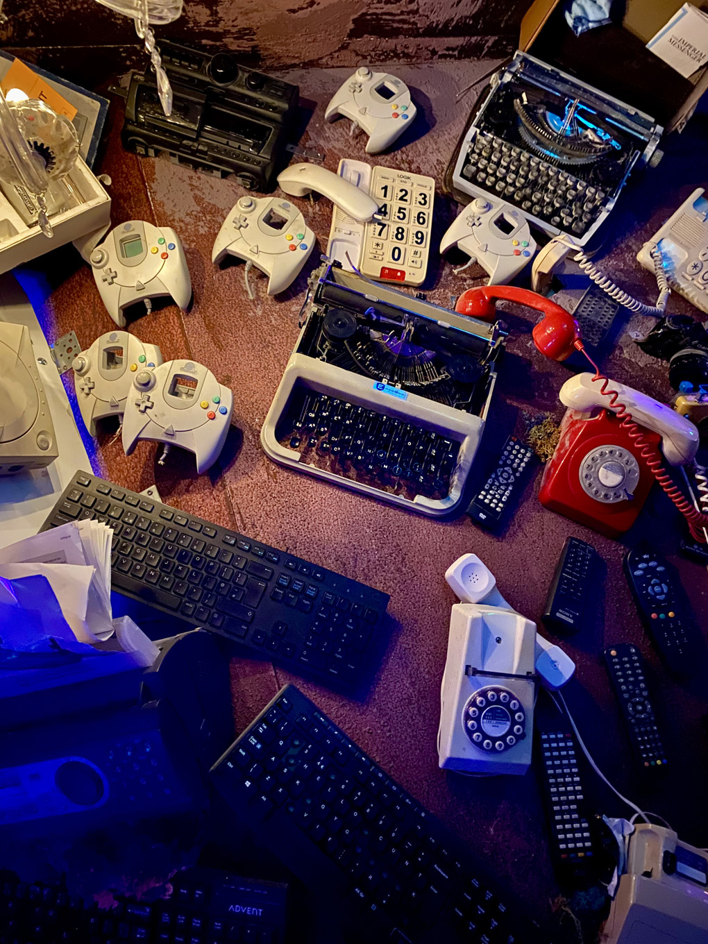 Typewriters, keyboards, rotary phones, game controllers, and TV remote controls stuck on a red wall.