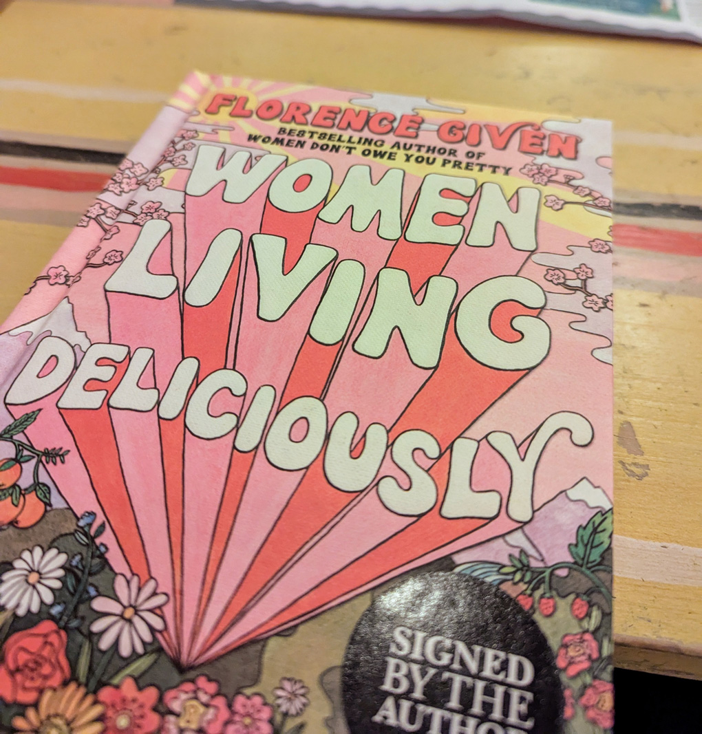 The cover of a book titled 'women living deliciously' placed on a table in a restaurant
