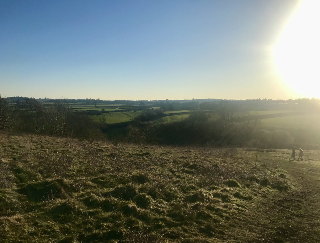 Sun setting in a blue sky, going down over green country hillside.