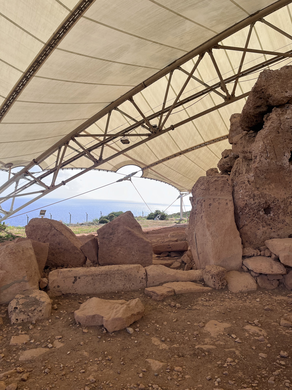 Several large and chiselled limestone rocks show where the outer wall would have been on the temple. A large tent-like canopy is also visible, with the sea in the background.