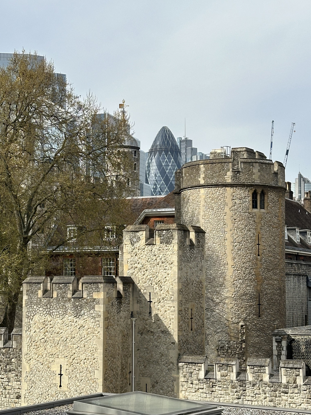 Three turrets of the Tower of London in ascending height from left to right. Gherkin building in distance visible behind and on top of middle turret.