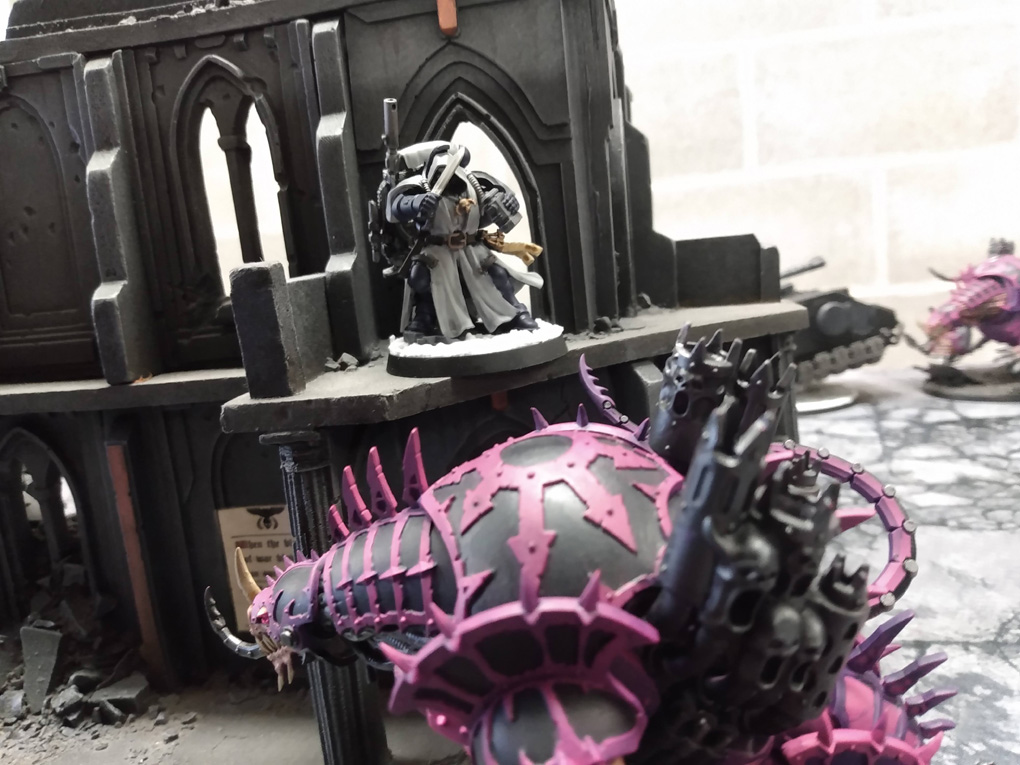 A miniature space marine stands on a ledge above his monstrous foe