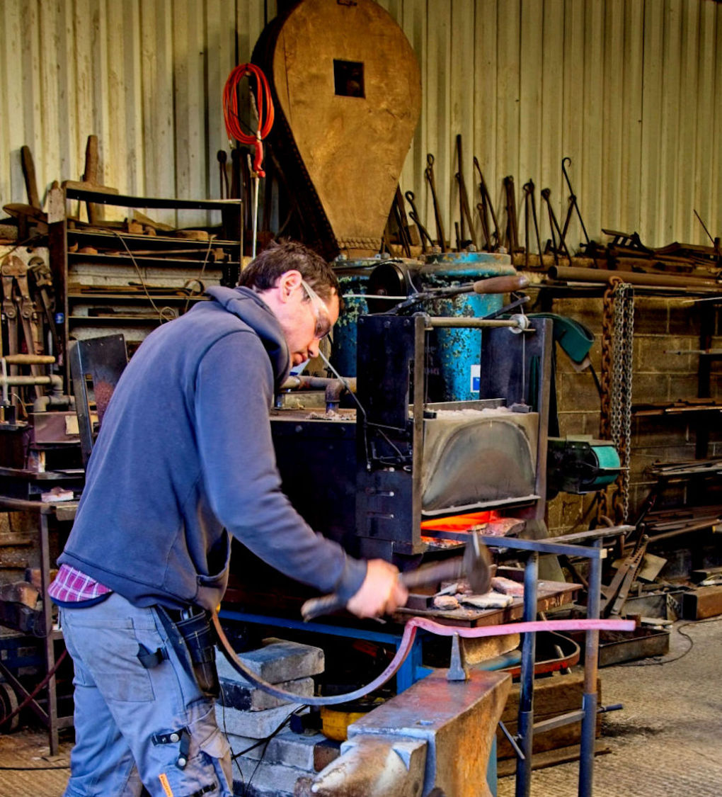 In the foreground the blacksmith is hammering on the curved piece that will hold the lamp in the arch over the new gateway for the church path.