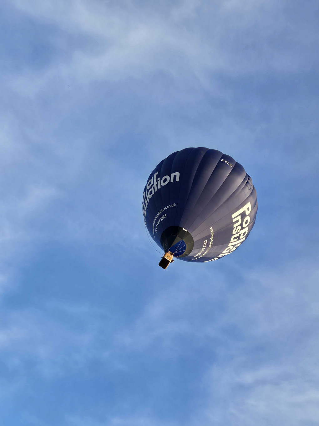 Looking almost directly upwards at a black hot air balloon in a blue sky that is streaked with white clouds. It looks like it is flying up towards the top right corner of the frame.