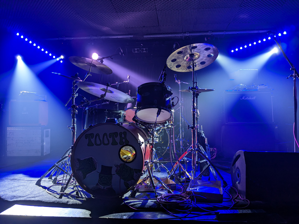 A drum kit on a dark stage crossed with spotlight beams