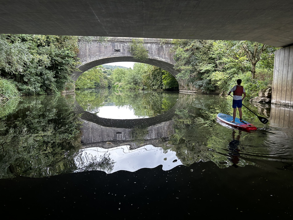 Man paddle boarding down a quiet river with lots of reflections of nature