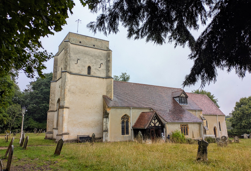 An old square towered church in a wooded churchyard on a rainy day