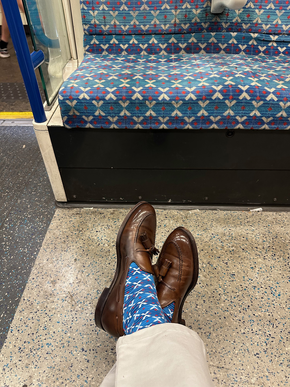 Crossed feet on Victoria line tube train with brown tassel loafers and beige chinos. Socks have same blue and white pattern as train seats.