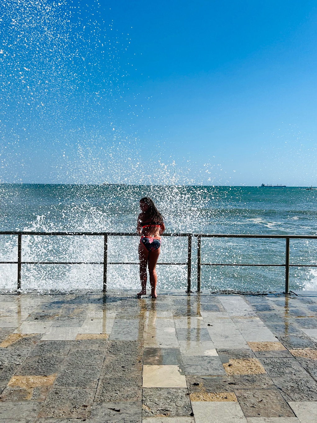 Waves splashing over a teenage girl standing on the side of a harbour on the Atlantic coast