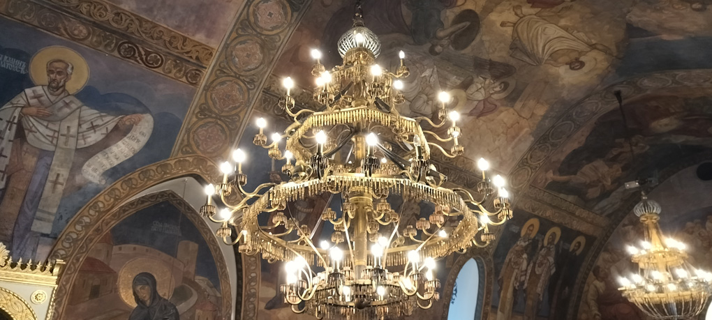 A chandelier in a small but very ornately designed Orthodox Church. The ceiling is painted with saints and religious images. The chandelier looks, at first, like a normal one with candle-shaped lightbulbs, but on closer inspection, the “chains” between the sections are made from bullets and the centre is made from blades, swords and bayonets.