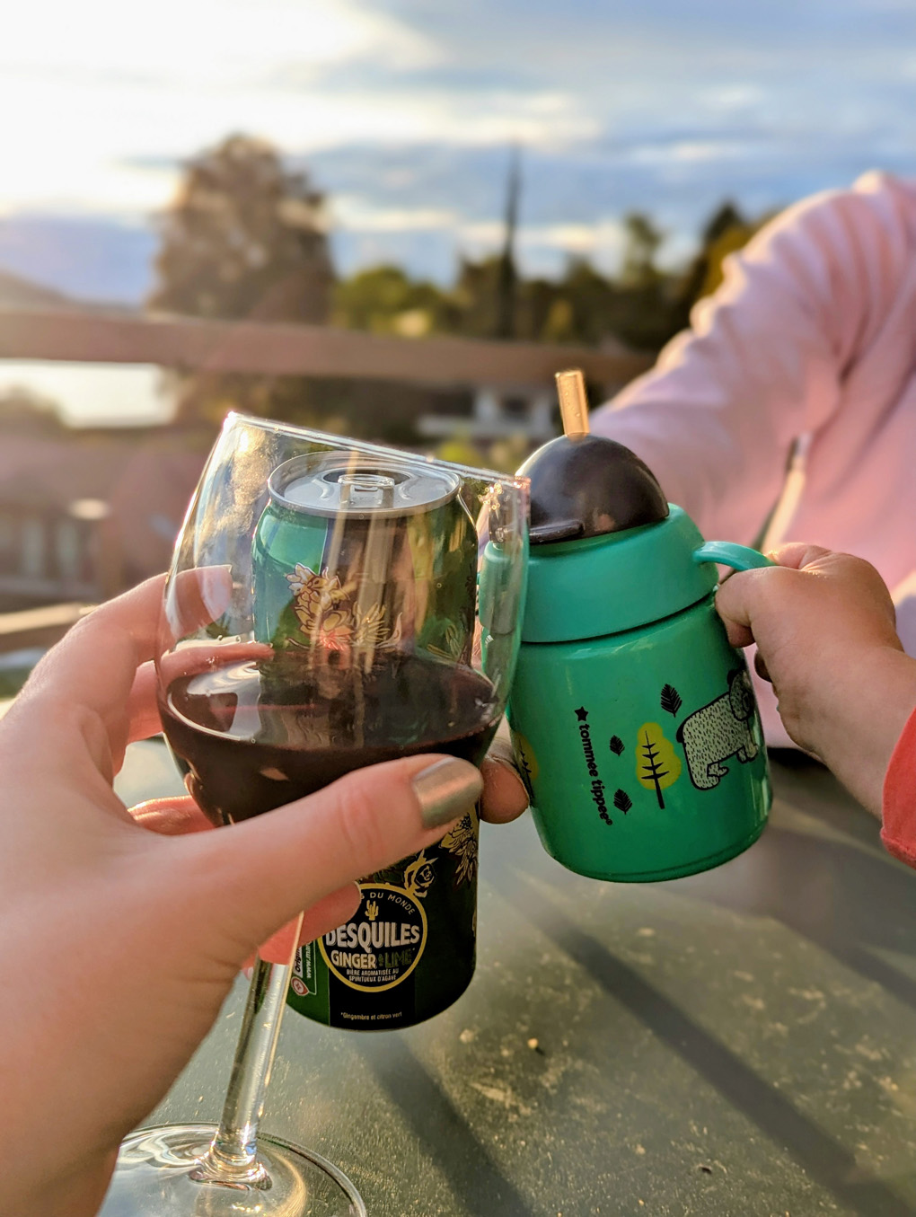Three hands bringing together a glass of red wine, a can of beer, and a little toddler's cup in a 'cheers' motion