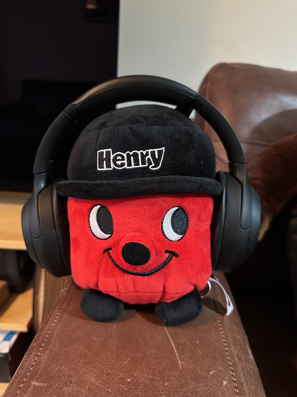 A Henry vacuum cleaner pushie toy with headphones on. On armrest of leather sofa.