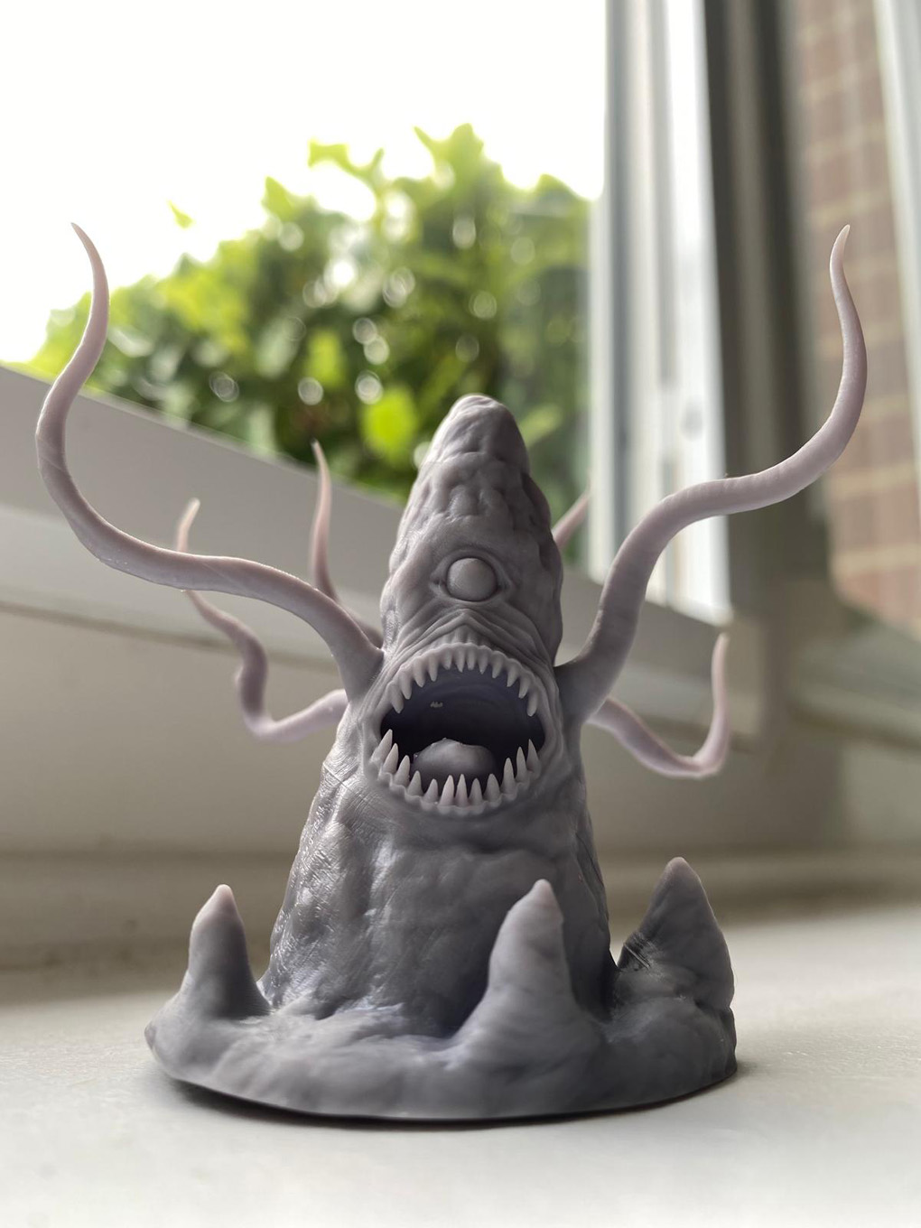 A grey 3D-printed model of a roper: a toothed rock with a single eye and flailing tentacles.